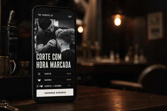 Telefone em pé num balcão de madeira mostrando o site de uma barbearia fictícia: foto em preto e branco de um corte em andamento, o título “Corte com hora marcada”, três serviços com duração e um botão de agendar horário.
